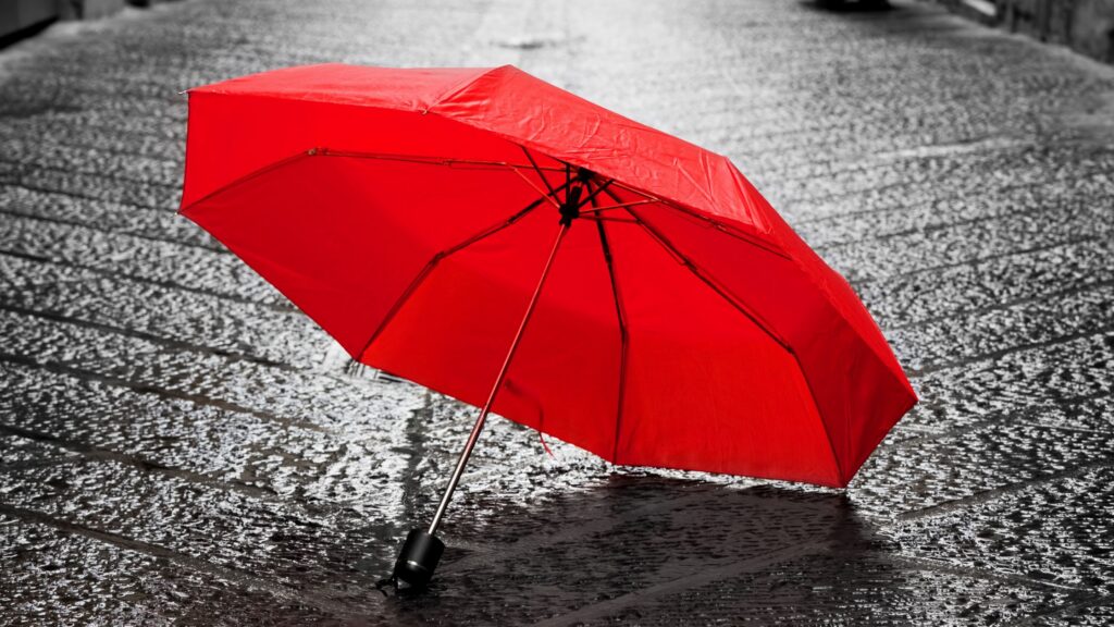Ein einzelnen roter Regenschirm auf einer grauen Gasse.