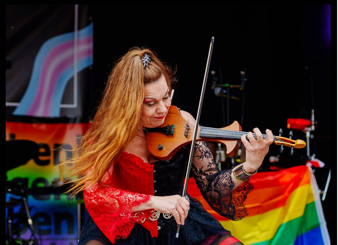 CSD Bielefeld. Sexarbeiterin Madame Kali alias Hexengeige spielt auf der Bühne vor Pride-Flagge